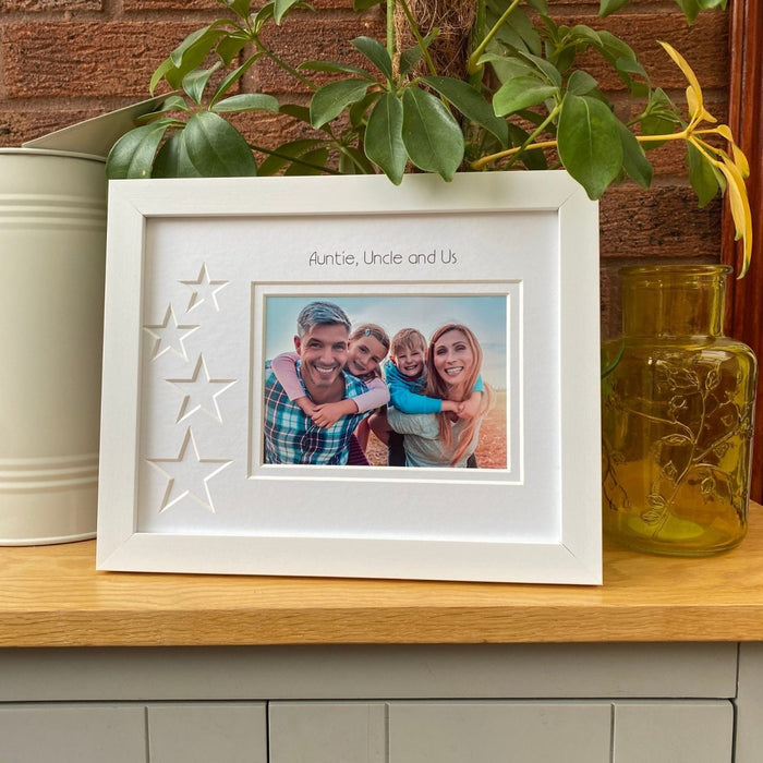 White frame on brown tabletop next to green plants, cream jug and yellow vase